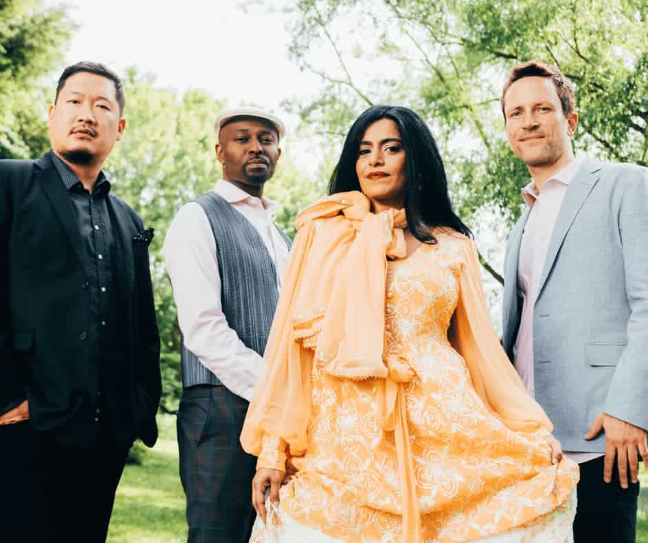 Three men and one woman stand underneath trees