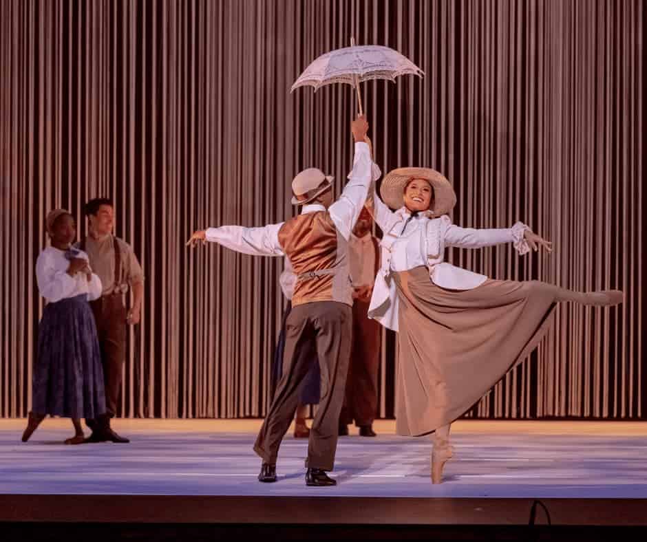 People dancing in early 20th century clothes and holding a parasol