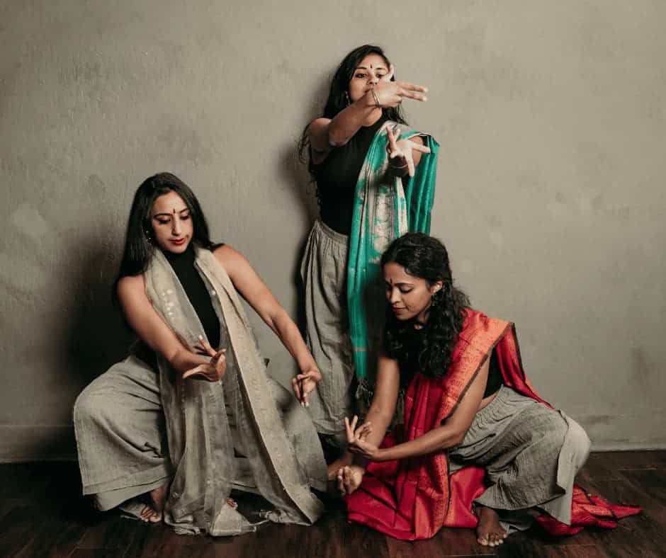 Three women in traditional Indian costume with bindi making gesture with their hands.