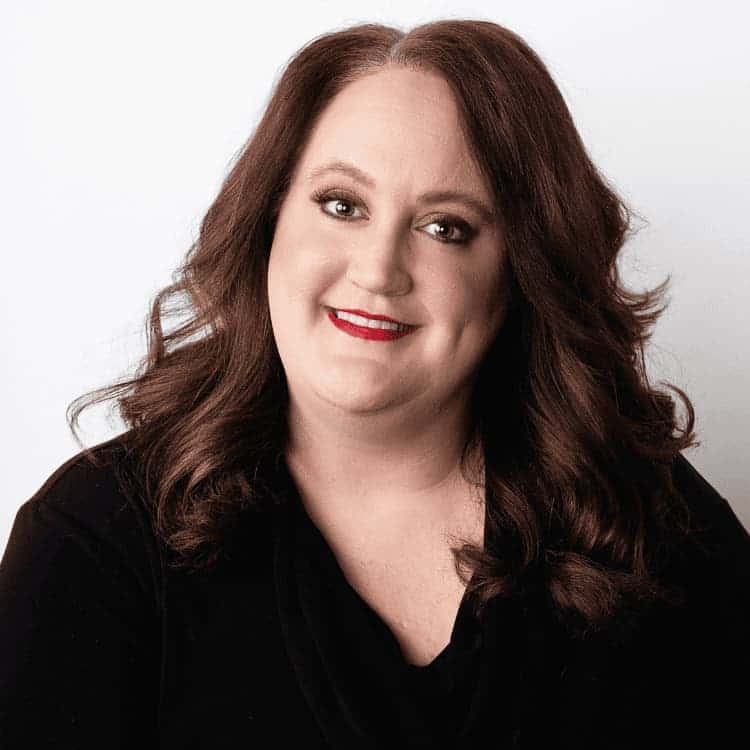 Individuals with long redish-brown hair smiles at the camera wearing red lipstick