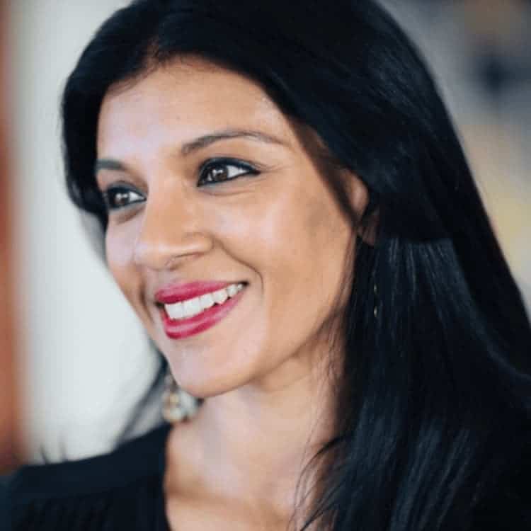 Female with black hair and red lipstick gazes into the distance with a smile