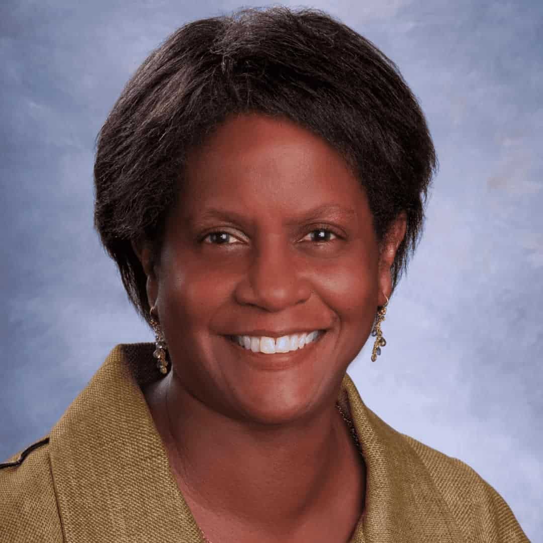 Brown skin, short dark hair and eyes, dangling earrings and light green jacket; photo by Margo Schulman.