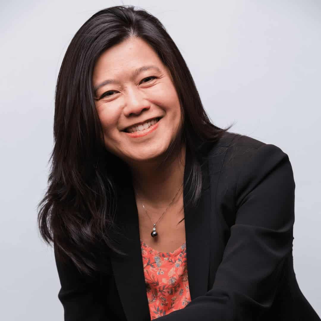 Amy is sitting with her hands on her legs. She is smiling with her head tilted to the right. She has medium length black hair with fair skin and is wearing a black jacket; photo by Robert Torres.