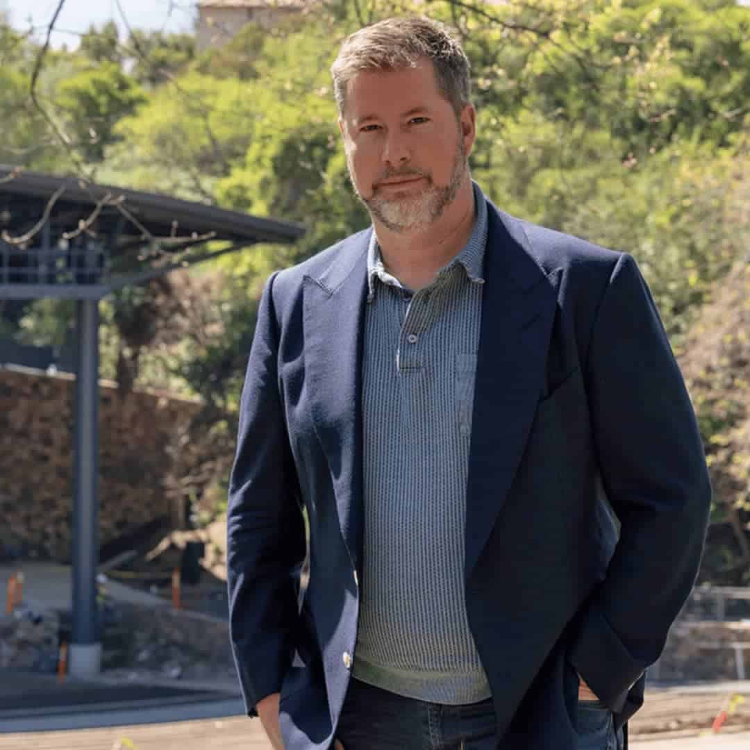 Chris standing in front of the Frost Amphitheater at Stanford. He is wearing a green collared shirt and a blue blazer. He has grayish blonde hair and brown eyes; photo courtesy of Stanford.