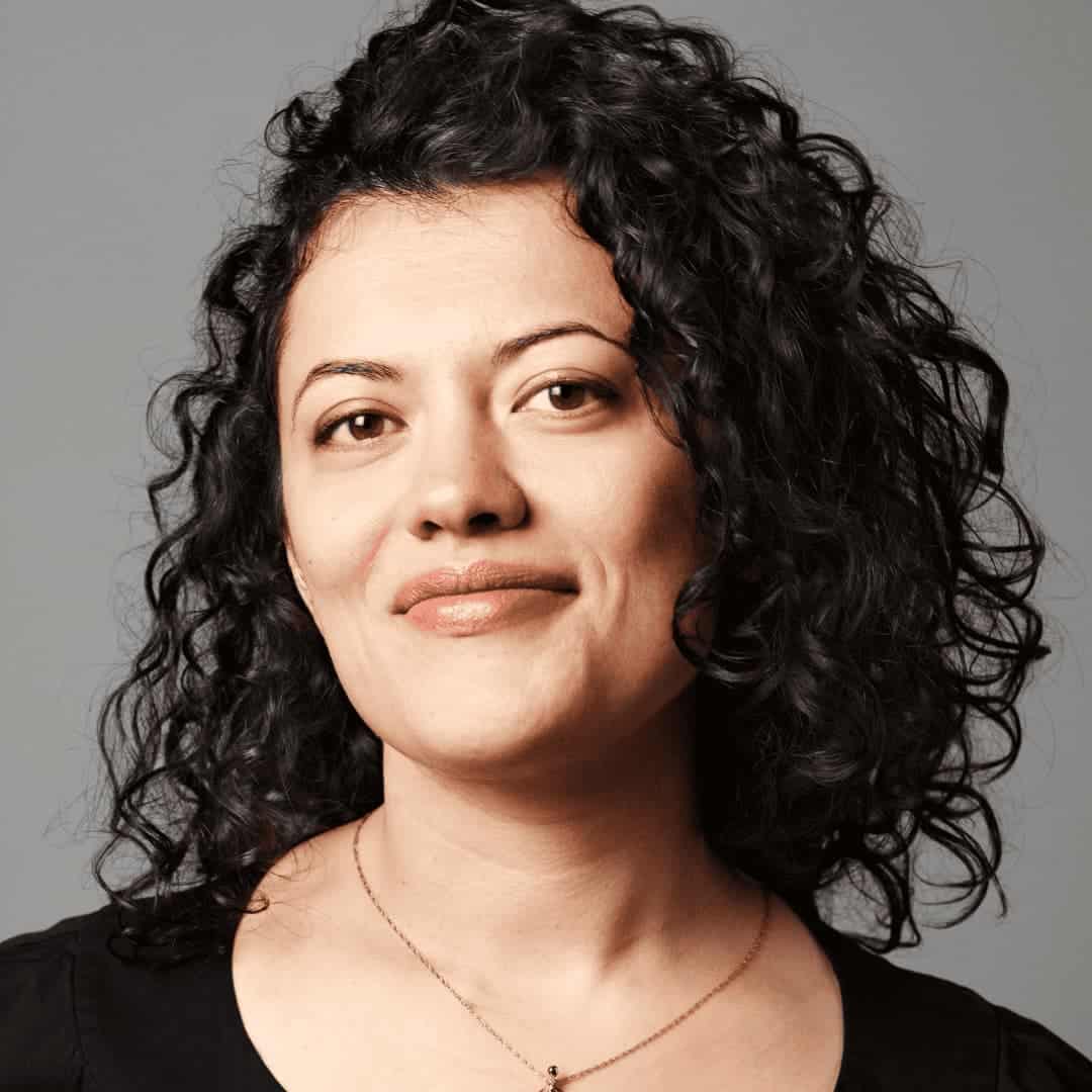 Shanta is smiling softly. She is fair-skinned, wearing a black shirt, and has mid-should black curls. Photo by Gregory Kramer.